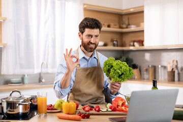 Fototapeta na wymiar Glad millennial caucasian male cooking eat show salad and ok hand sign at table with vegetables and computer