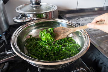 Cabbage cut into strips being prepared in a large frying pan that is on the stove
