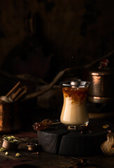 Masala tea on wooden podium with cardamon,cinnamon sticks,anise stars and milk.Helthy,vegan drink in rustic style.
