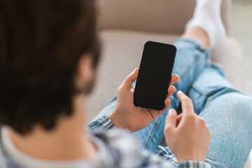 Cropped young caucasian guy sit on sofa, chatting on smartphone with empty screen, surfing internet, reading news