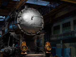 Obraz premium Old black steam engine train in a hangar with beautiful lighting brass lamps
