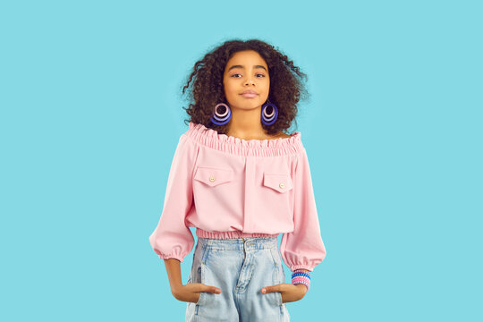 Portrait of beautiful stylish african american preteen girl on light blue studio background. Confident ethnic smiling kid girl with curly hair dressed in stylish teenage clothes and female accessories