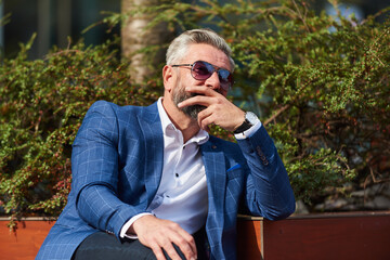 Modern senior businessman resting on a bench in the city on a break from work