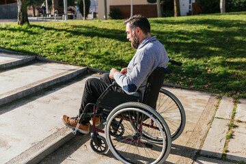 Man in a wheelchair facing accessibility problem in front of the stairs of the park.