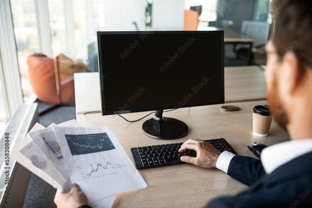 Poster Unrecognizable male employee using computer with blank screen and working with documents at desk in office, mockup