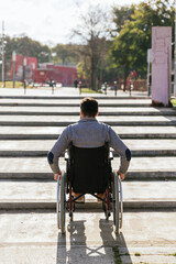 Obraz premium Man in a wheelchair faced with an accessibility problem on the stairs in the park.