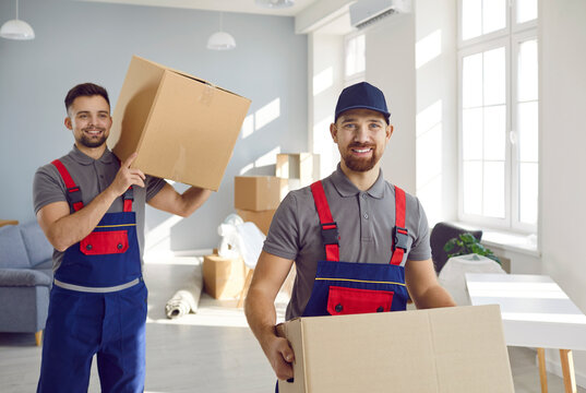 Delivery, moving, forwarding, loader or courier. Two smiling delelivery men or transportation workers carry cardboard boxes for moving to apartment. Male employees of company moving in overalls.