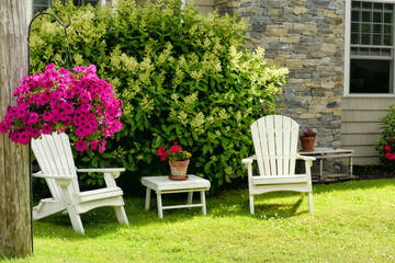 Resting place in the garden near the house. Traditional wooden armchairs and flowers. Selective focus on flowerpot with petunia flowers.