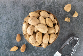 Shelled almonds in a wooden bowl, almond kernels and a nutcracker on a gray background, top view. Selective focus