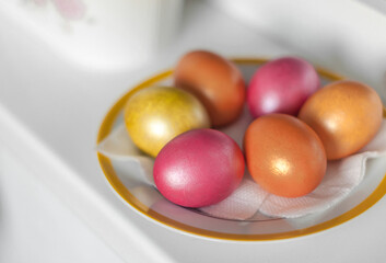 Orange, pink and gold Easter eggs on a plate with a yellow border top view.