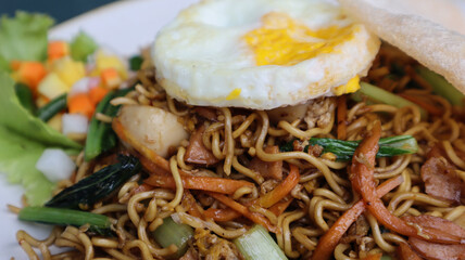 Asian authentic fried noodle with meat ball, veggie, shrimp crisp and egg in a plate.
