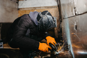 worker man in a welding mask welds metal in the back of a van