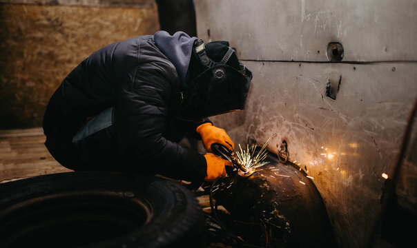 worker man in a welding mask welds metal in the back of a van