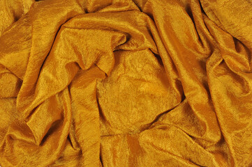 Crumpled soft fabric waved background in yellow -gold color with shiny effect . top view