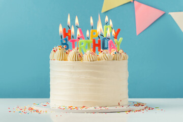 Birthday cake with white cream cheese frosting decorated with multicolored lit happy birthday text...