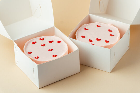 Little Korean style pink bento cake with hearts in a white box on the beige background.  Pastry as a gift for a birthday of beloved one. Present for Valentine's Day