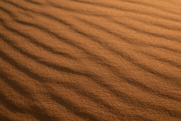 Fototapeta na wymiar Incredible wavy diagonal patterned textured sand waves on a desert or beach with beautiful golden light running across tiny pebbles specks of sand.