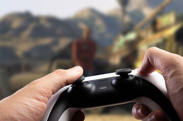Video games. A gamepad in the hands of a gamer against the background of a video game on a large TV screen. Modern technologies, electronics, video games, online games with friends. © Anton