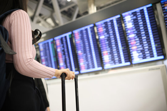 Female Tourist holding Passport Air Ticket with Luggage at International Airport . Tourist check air flight from flight information board , Travel and Business concept