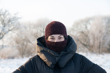 Fototapeta na wymiar Beautiful girl in a brown balaclava. Fashionable hat on a beautiful woman. BALACLAVA GOOD PROTECTION FROM FROST AND WIND