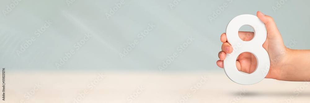 Aufkleber Eight in hand. A hand holds a white number 8 on a blurred background. Concept with number eight. Birthday 8 years, percentage, eighth grade or day, international women's day.