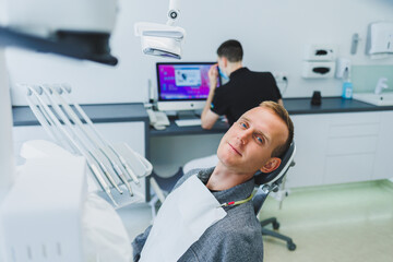 A young man is sitting in a dental chair, and a dentist is working at a computer. Dentist's appointment