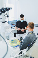 Obraz premium A dentist in a modern dental office tells a patient about dental care. A man sits in a dental chair and listens to a dentist.