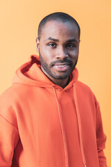 The portrait of a dark-skinned man in an orange hoodie, Black guy fashion. Orange background.