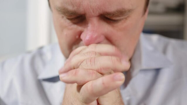 Portrait of serious man praying with his hands folded on in prayer in hope asking of help.