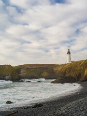 Lighthouse on the high shore of the ocean. Cloudy sky, gray sea water. Historical place, excursions, tourism, architecture. There are no people in the photo.