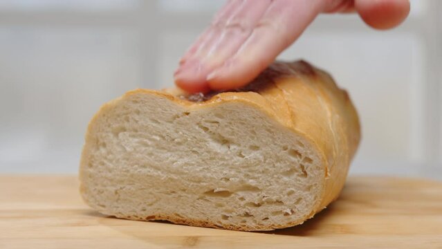 Fresh wheat bread on  wooden board close-up. Female hand pressing on loaf of white bread, freshness check. 