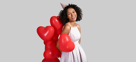 Happy African-American woman with heart-shaped balloons on light background