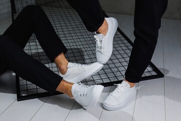 Close-up of male and female legs in black pants and white casual sneakers. Summer men's and women's...