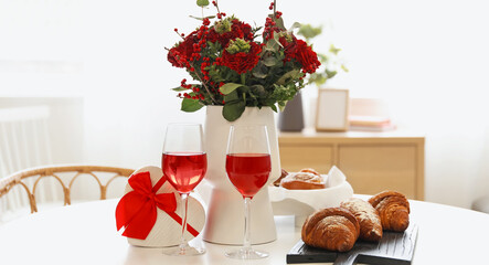 Vase with beautiful bouquet of flowers, pastries, glasses of wine and gift for Valentine's Day celebration on dining table in room