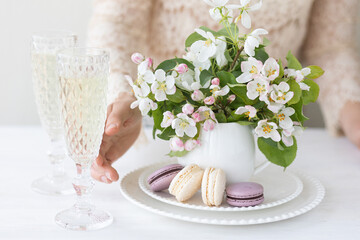 Beautiful composition with delicious French macarons and spring flowers in a white cup. Young beautiful girl in a lace dress holding a plate with sweet dessert and apple tree flower. Bride's morning