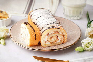 Plate with delicious sponge cake roll and floral decor on white table