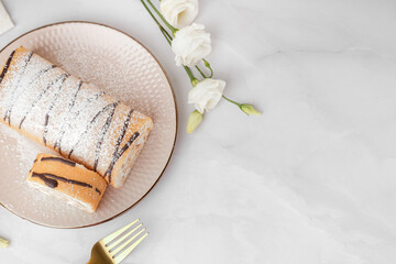 Plate with delicious sponge cake roll and floral decor on white table