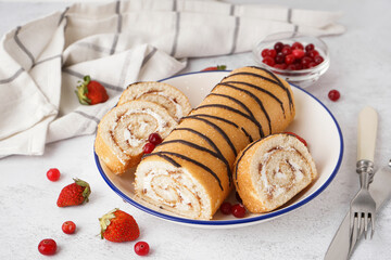 Plate with delicious sponge cake roll, fresh berries, cutlery and napkin on white table