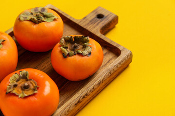 Wooden board with fresh ripe persimmons on color background, closeup
