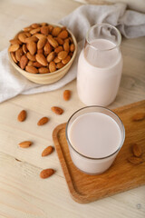 Board with glass, bottle of almond milk and nuts on wooden background