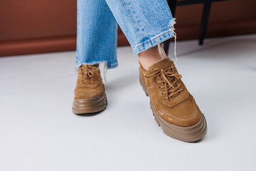 Close-up of female legs in jeans and brown casual suede sneakers. Women's summer shoes