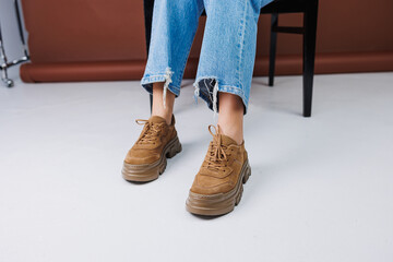 Close-up of female legs in jeans and brown casual suede sneakers. Women's summer shoes