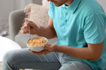 Young man eating cornflakes with spoon at home, closeup