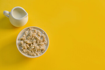 Bowl with tasty oatmeal and pitcher of milk on yellow background