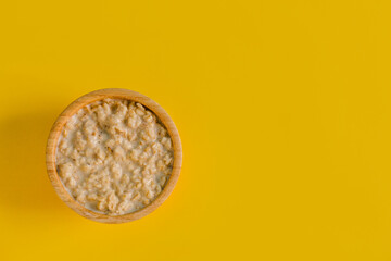 Wooden bowl with tasty oatmeal on yellow background