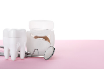 Plastic tooth with dental floss and tools on pink table against white background