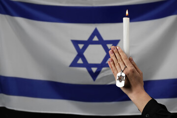 Woman with candle and military tag against flag of Israel. International Holocaust Remembrance Day
