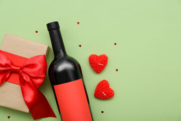 Bottle of wine with gift, candles and hearts on green background. Valentine's Day celebration