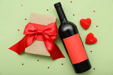 Bottle of wine with gift, candles and hearts on green background. Valentine's Day celebration