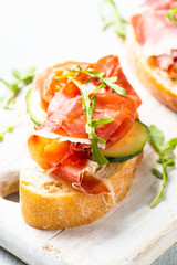 Open sandwiches with prosciutto and arugula on cutting board at white background. Close up image.